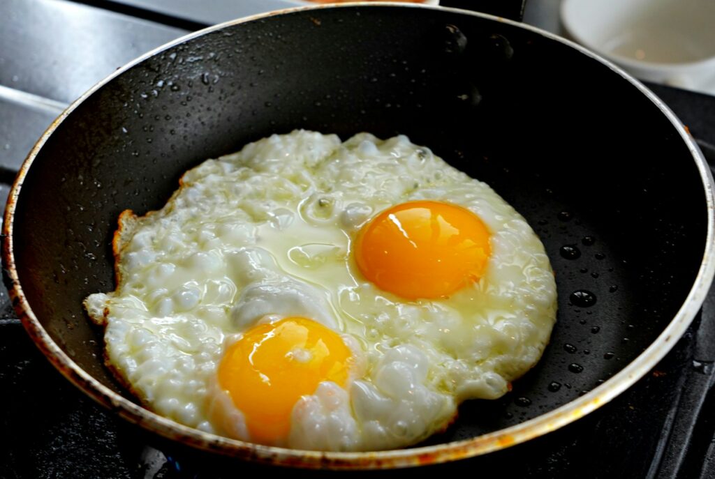 Two fried eggs cooking in a black frying pan